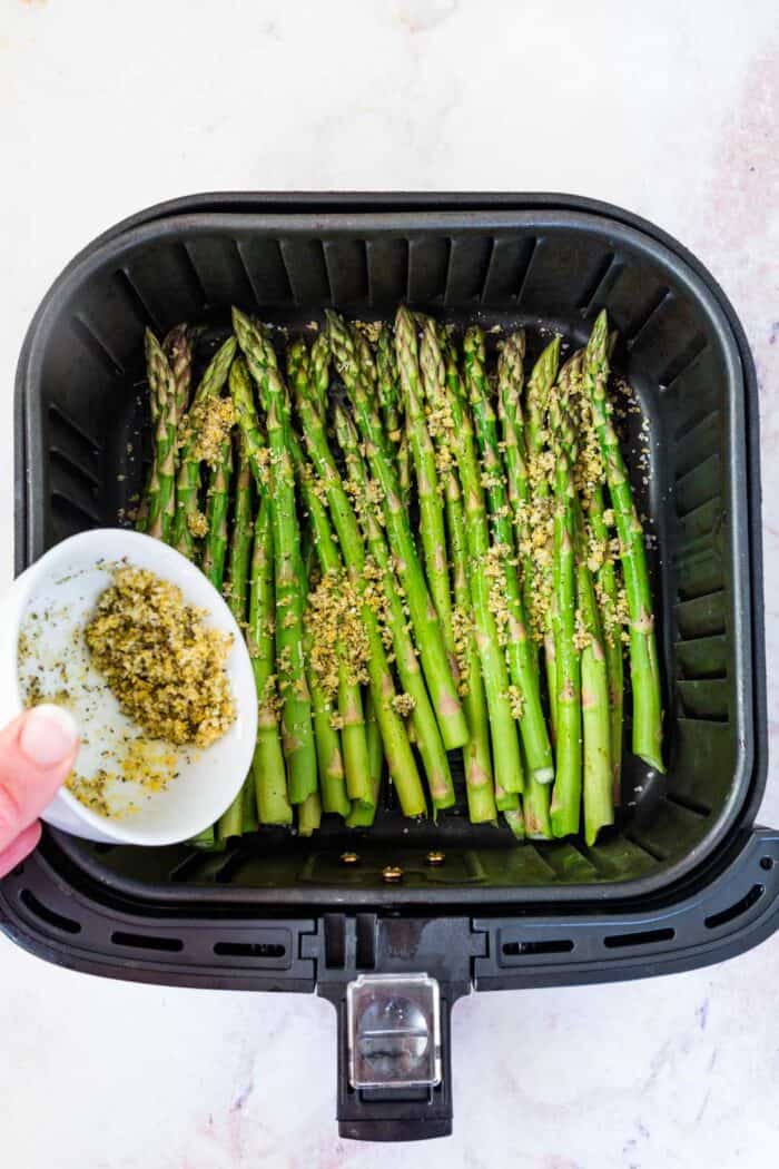 sprinkling crumb topping over raw asparagus in an air fryer basket