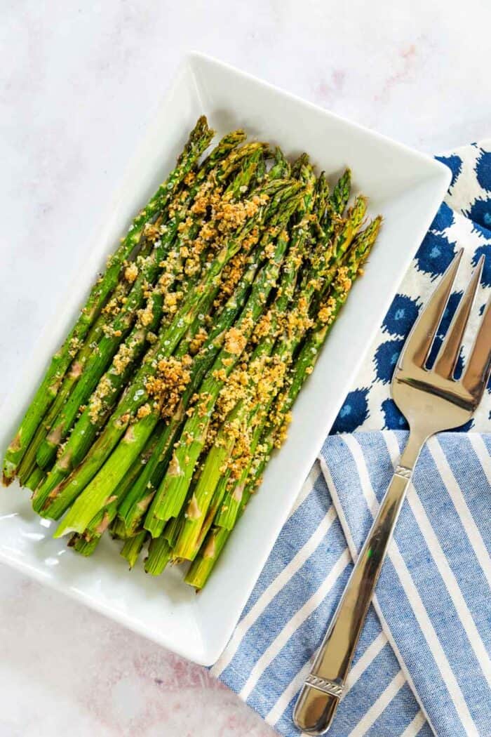 air fryer asparagus with parmesan herb crust on a white rectangular plate with a serving fork