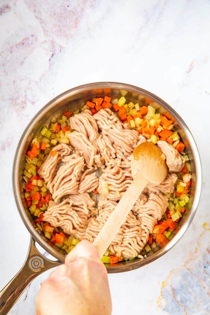 raw ground chicken added to the skillet with the carrots, celery, and onion bring chopped with a wooden spoon