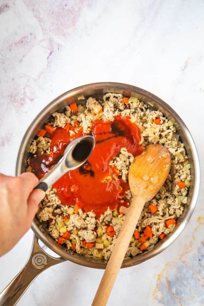 pouring worcestershire sauce over the tomato sauce and hot sauce that were added to the skillet with the ground chicken mixture