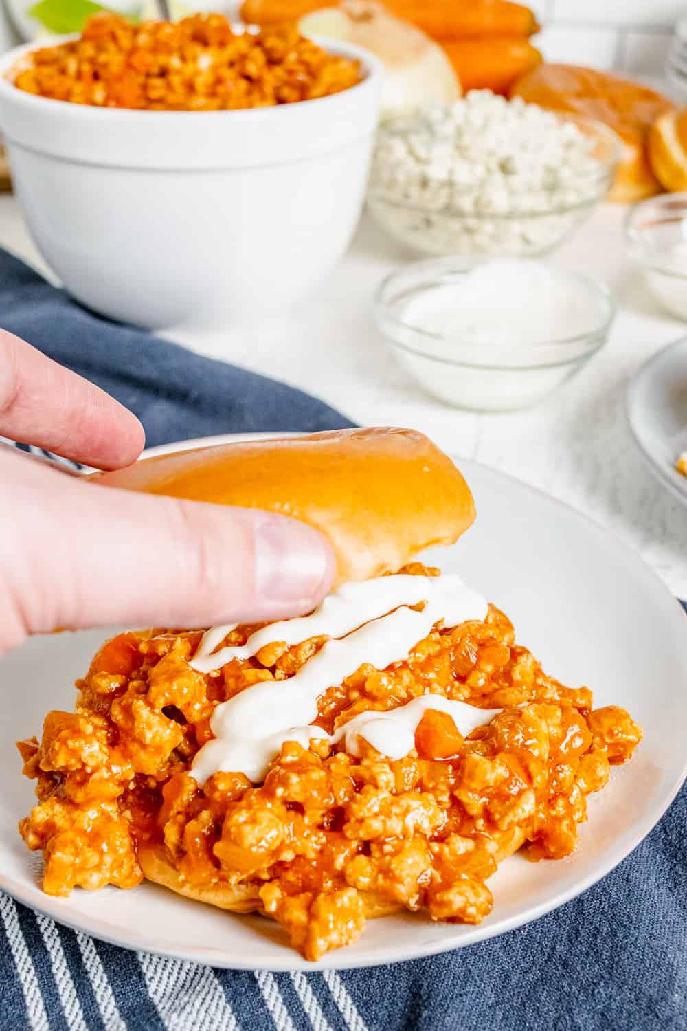 Putting the top of the bun on top of a buffalo chicken sloppy joe sandwich drizzled with Ranch dressing