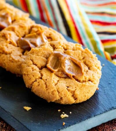 a slate platter with a lined up stack of dulce de leche peanut butter thumbprint cookies