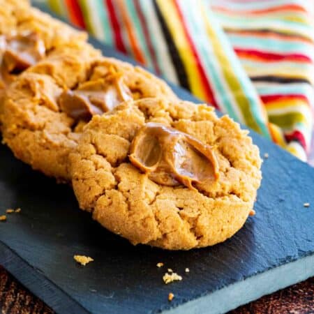 a slate platter with a lined up stack of dulce de leche peanut butter thumbprint cookies