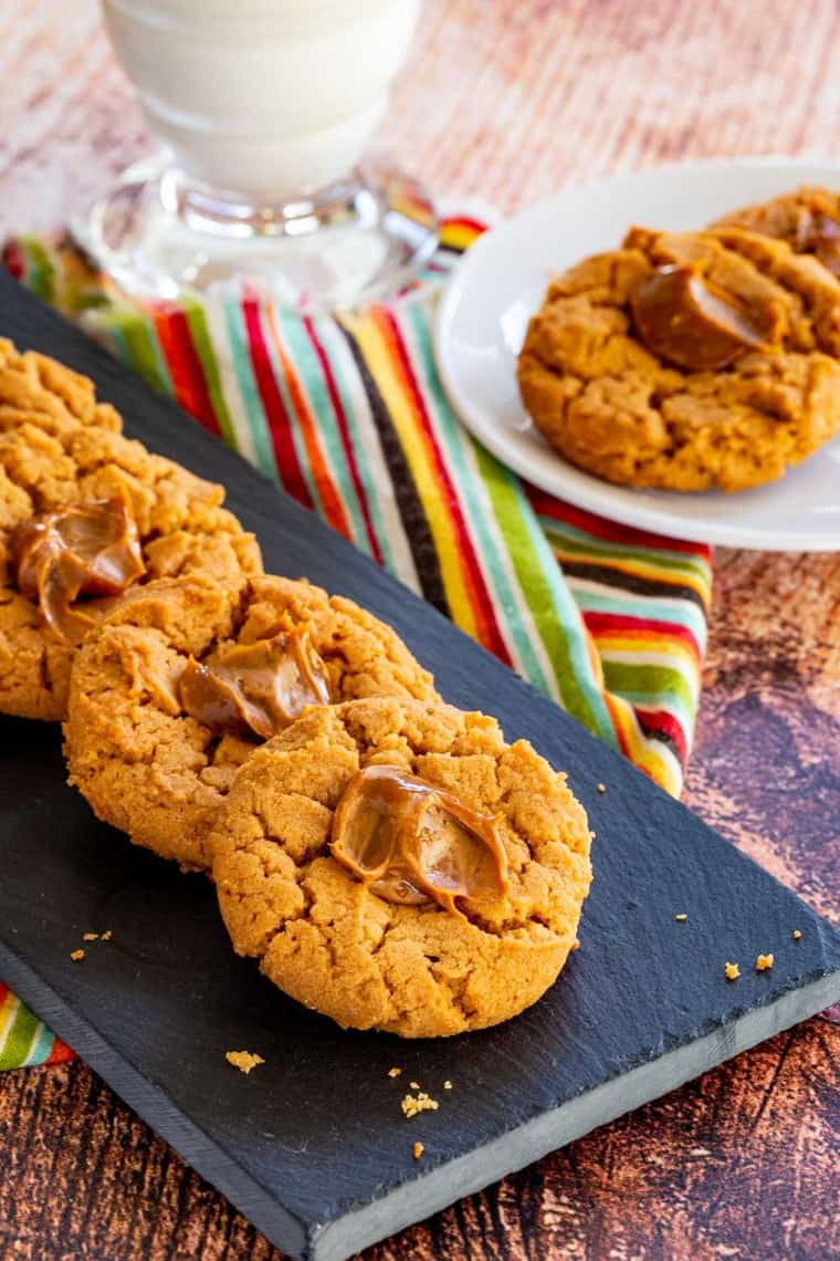 dulce de leche cookies lined up on a slate platter with two on a plate