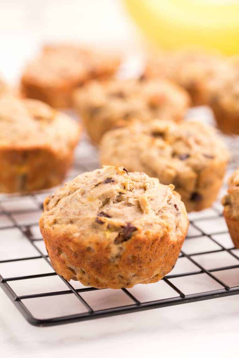 One gluten free banana chocolate chips muffin on a wire cooling rack with more behind it on the rack