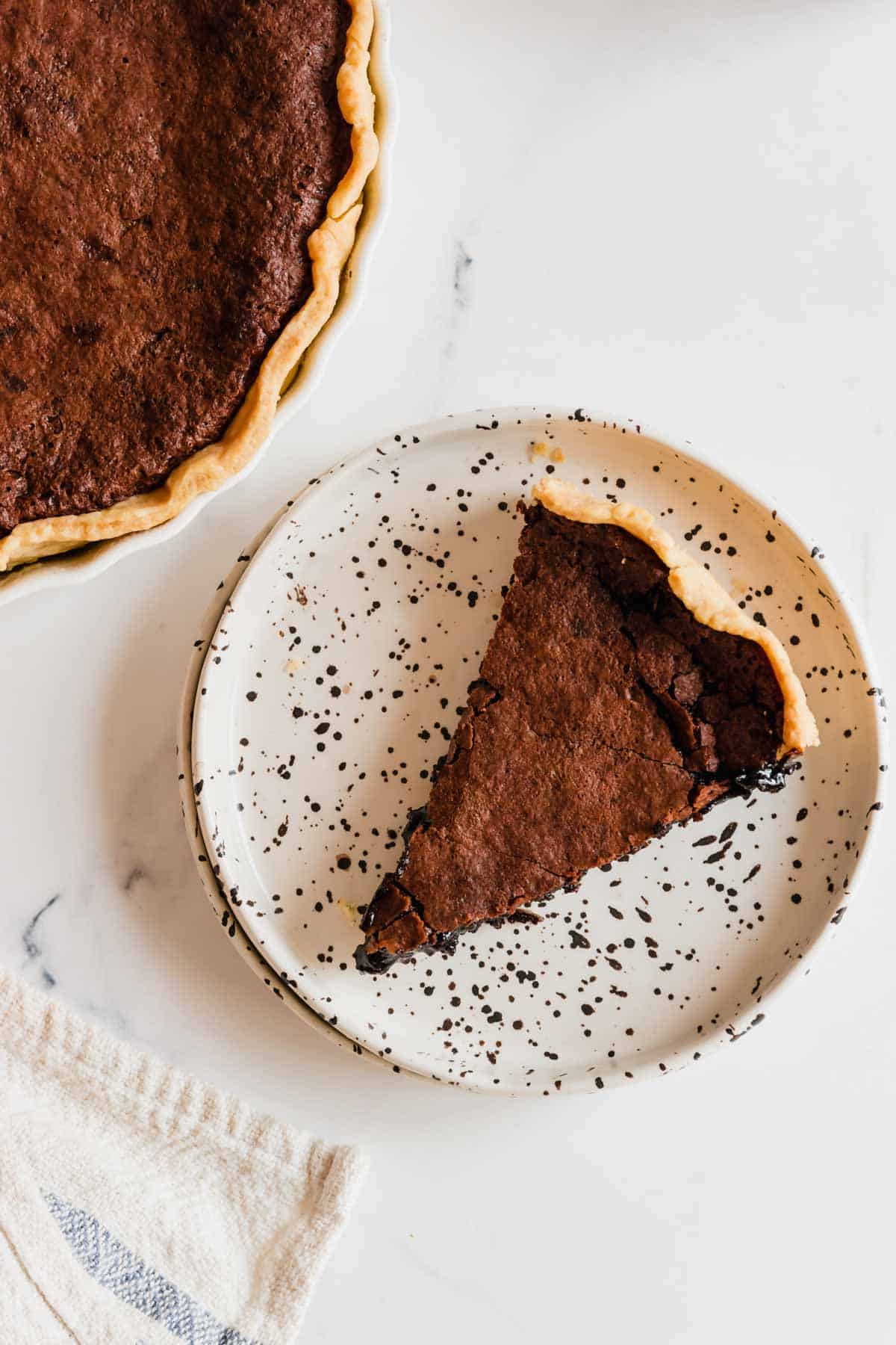 Looking down on a piece of chocolate pie on a speckled plate with the rest of the pie off in the corner.