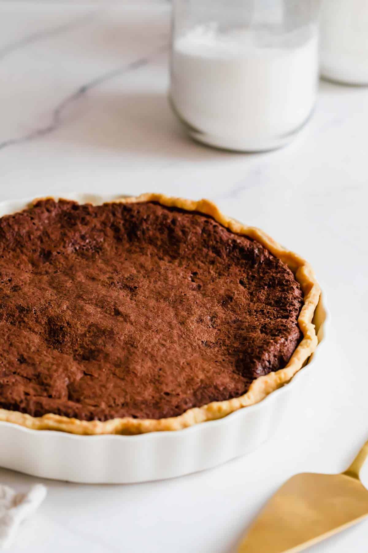 A Baked Chocolate Chess Pie on a White Marble Counter with a Glass of Milk