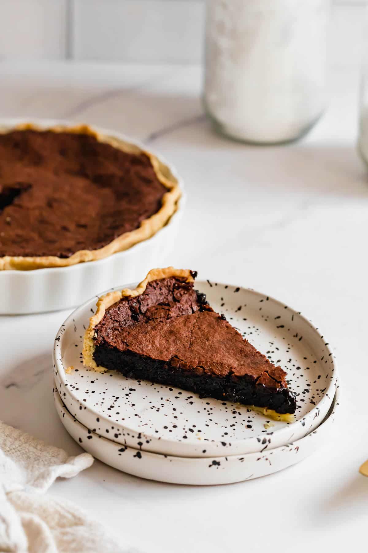 A Piece of Chocolate Pie on a Plate with the Full Chess Pie in the Background