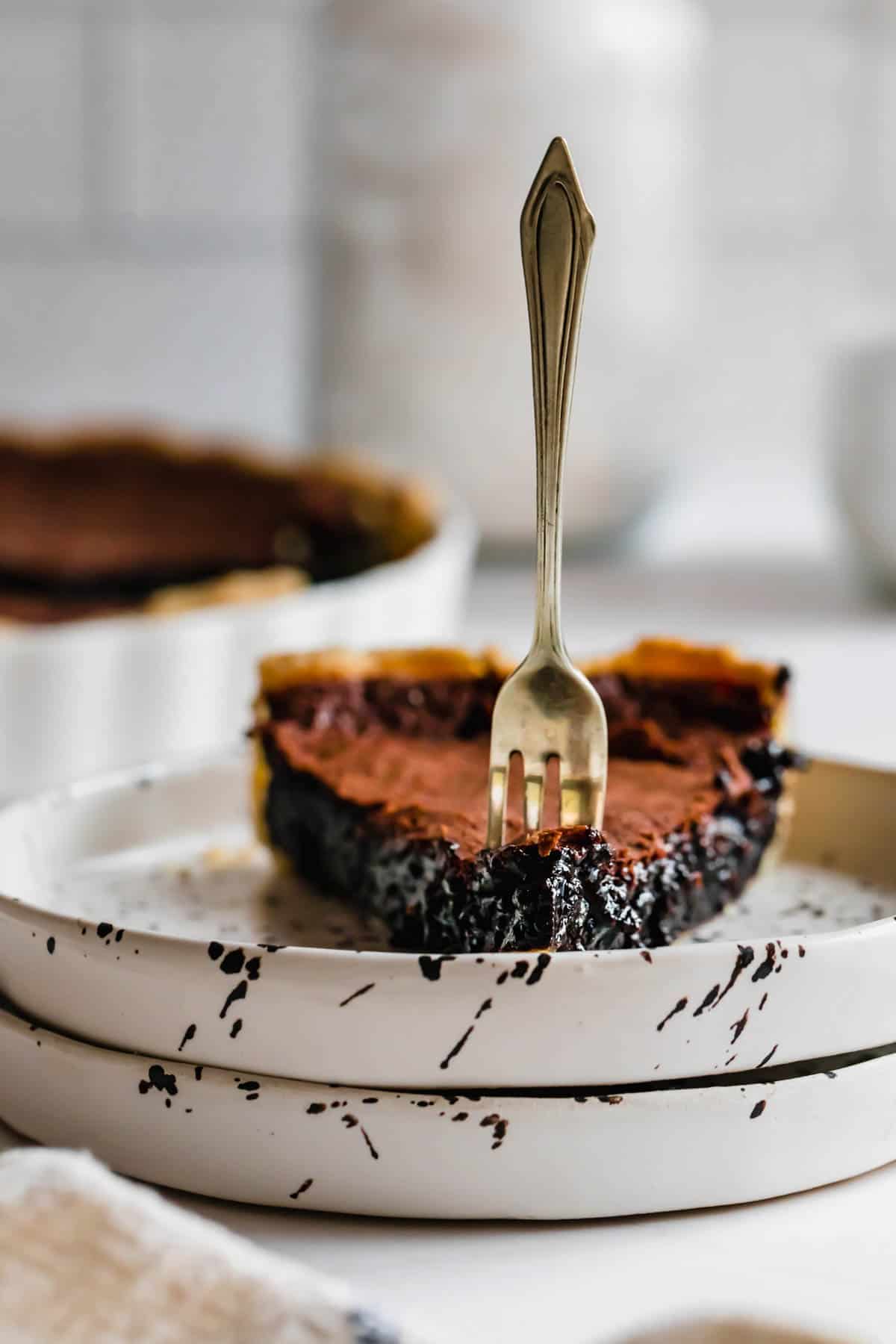 Two Stacked Plates Holding a Slice of Chocolate Chess Pie with a Fork Stuck Into it