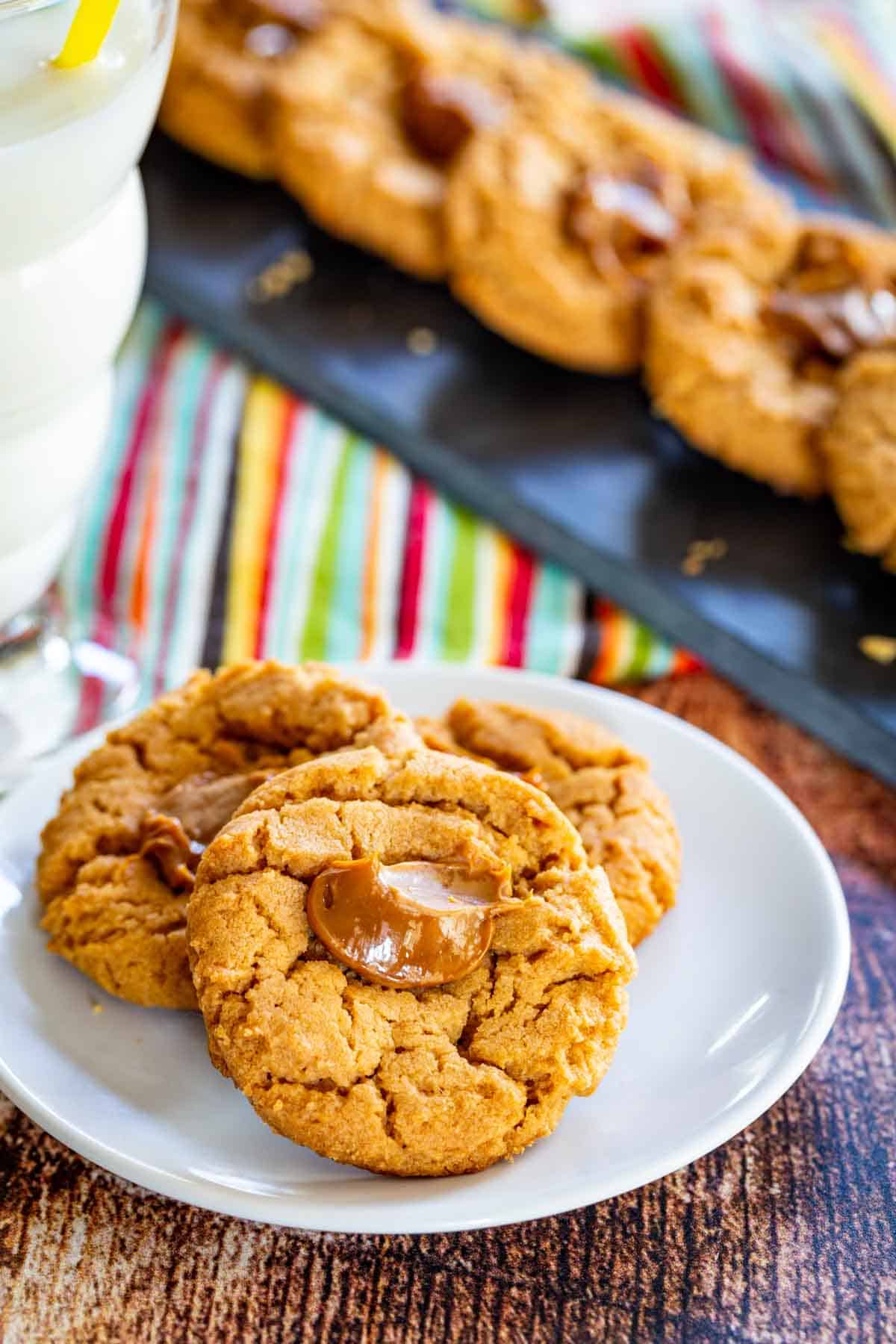 Three dulce de leche thumbprint cookies on a white plate.