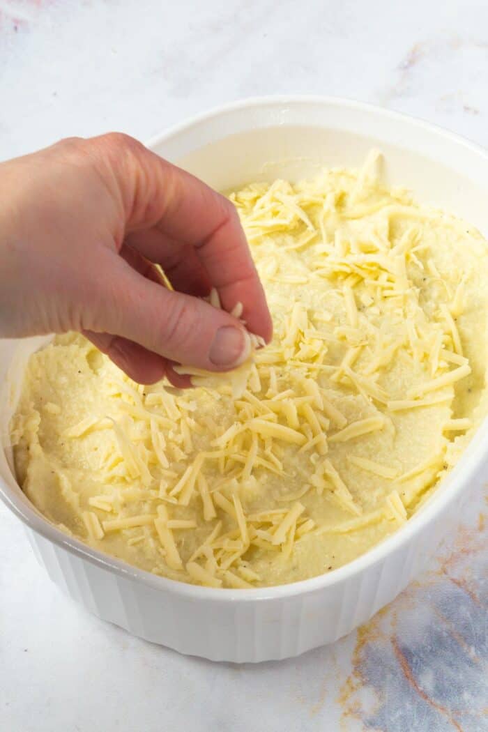 hand sprinkling shredded cheese on top of a mashed cauliflower casserole