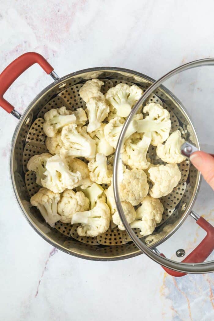 cauliflower florets on a steamer basket in a pot