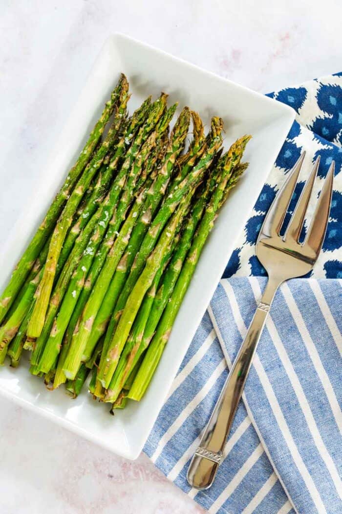 air fryer asparagus on a white rectangular plate with a serving fork