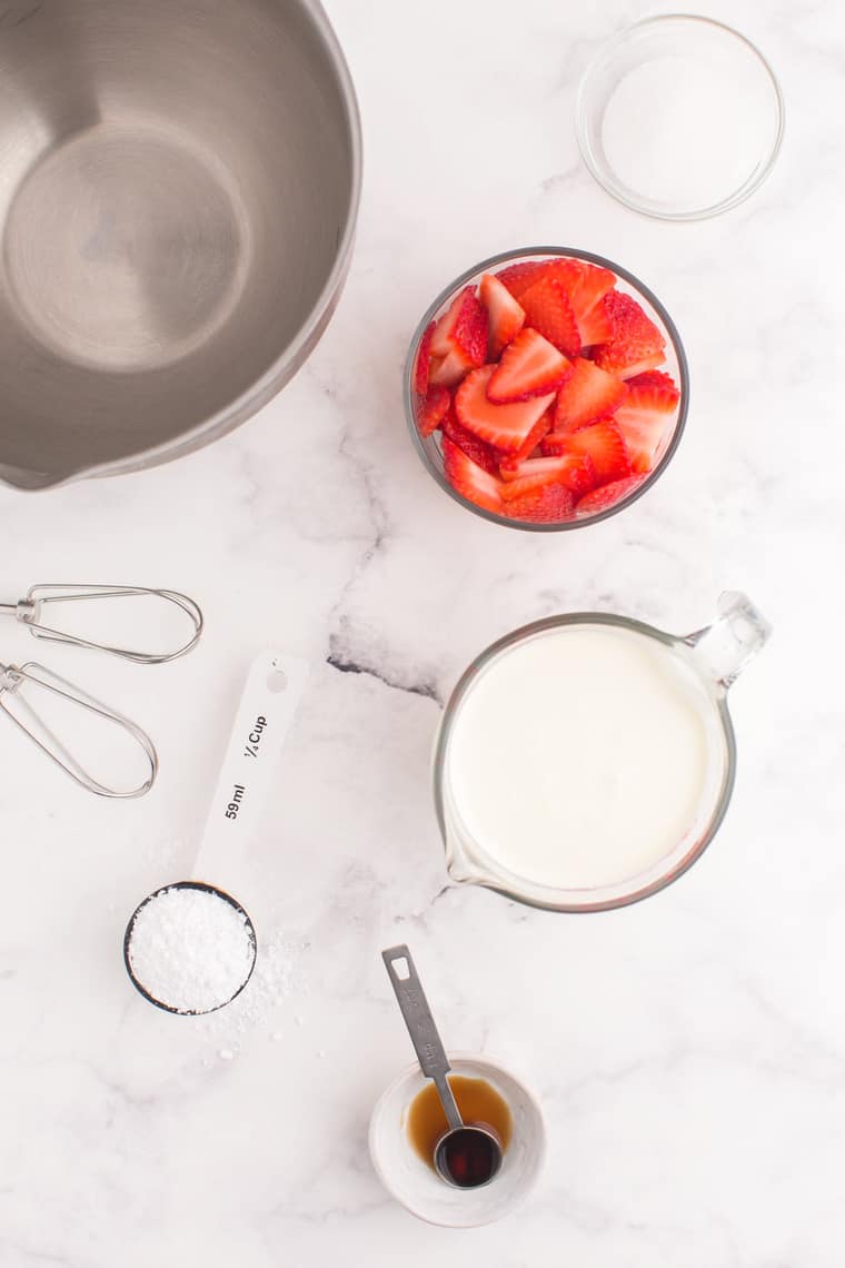 Strawberries, sugar, heavy cream, powdered sugar, and vanilla extract in bowls and measuring cups on a tabletop