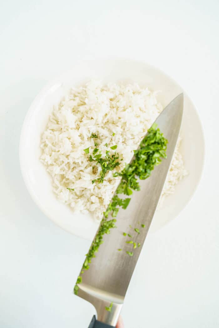A Kitchen Knife Pouring Fresh Chopped Cilantro Into a Bowl of White Rice