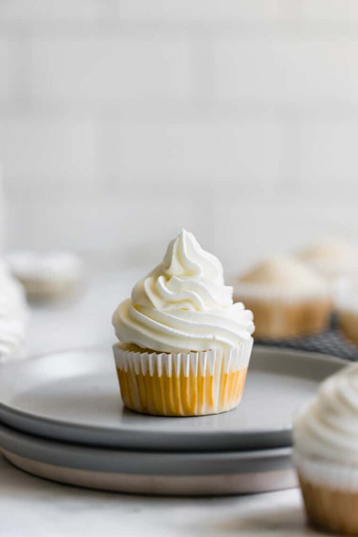 A Single Vanilla Cupcake with Vanilla Frosting on Two Stacked Plates