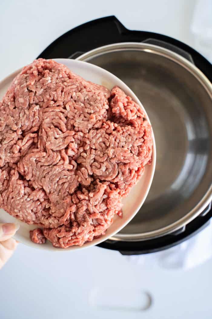A Plate of Raw Ground Beef Being Held Over an Empty Instant Pot