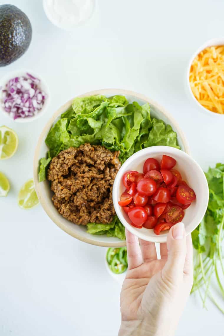 Sliced Cherry Tomatoes Being Held Over a Bowl of Lettuce and Ground Beef
