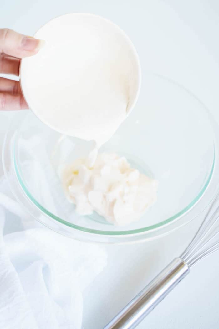 Cream Being Poured Into a Glass Bowl with Mayonnaise in It