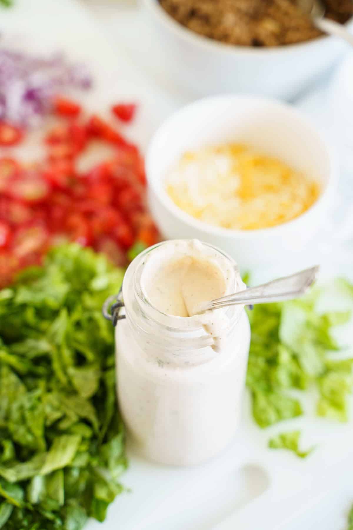 A Jar of Creamy Southwest Dressing Nex to to a Cutting Board Full of Salad Veggies