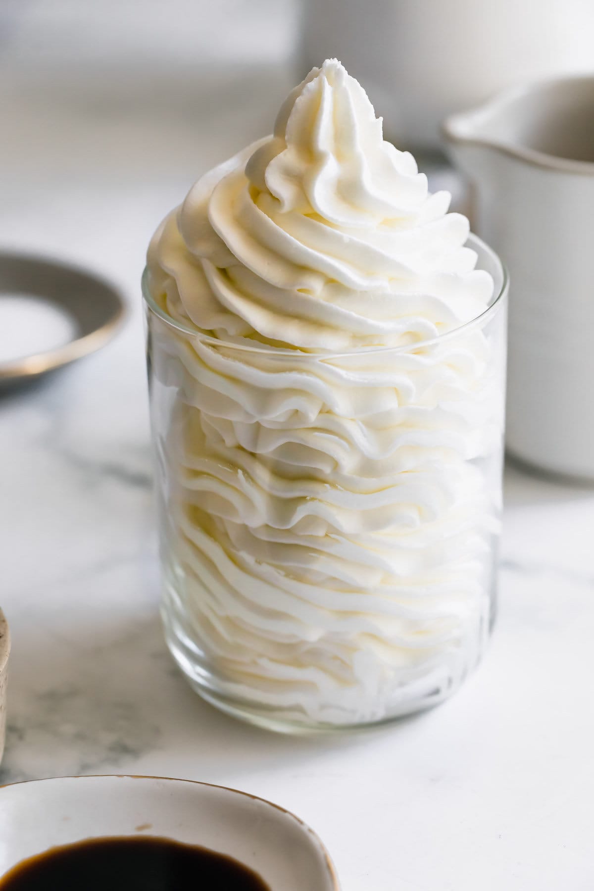 A Glass Cup Filled with Vanilla Frosting on a Marble Countertop.