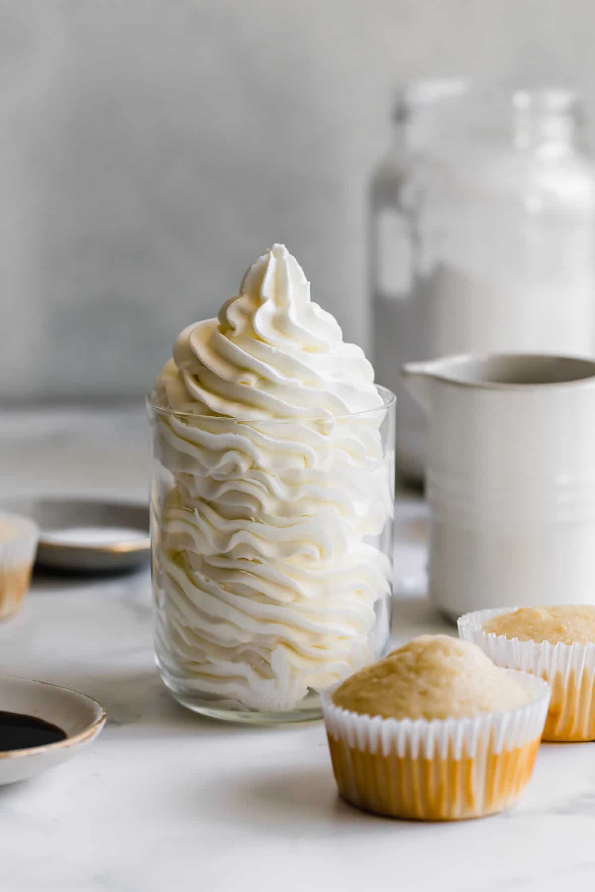 A Cup of Vanilla Buttercream Next to Two Unfrosted Vanilla Cupcakes.