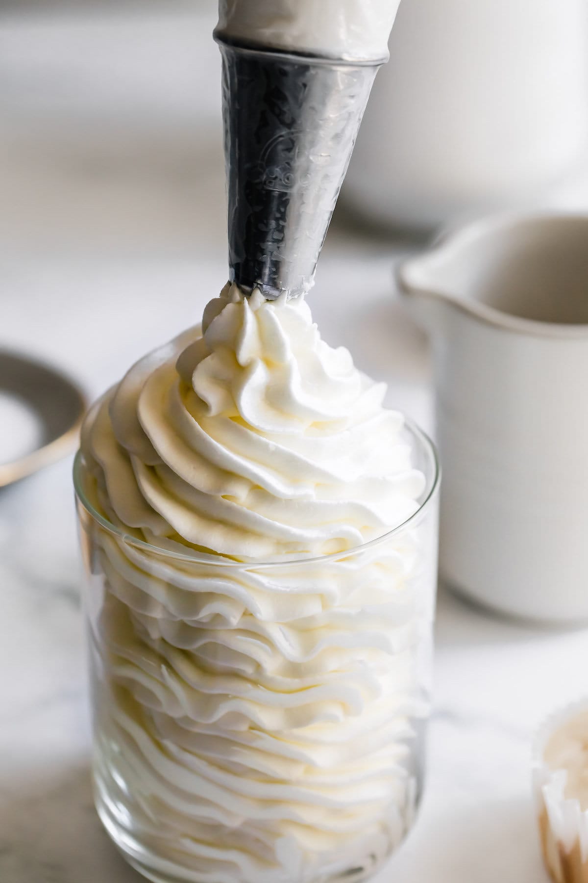 A Piping Tip Full of Vanilla Buttercream Piping the Frosting Into a Glass.