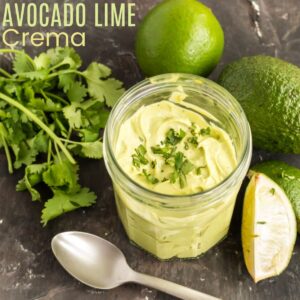 jar of avocado lime crema surrounded by an avocado, limes and a bunch of cilantro