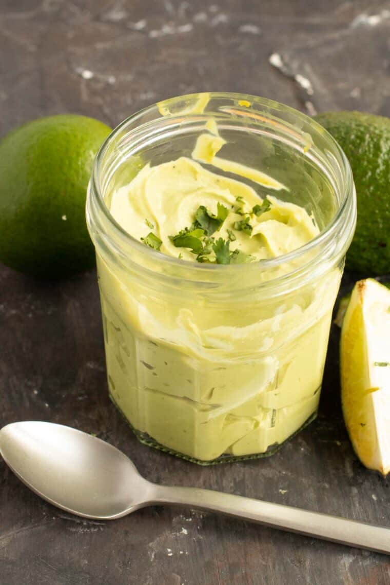 Avocado cream in a glass jar with a spoon in front of it