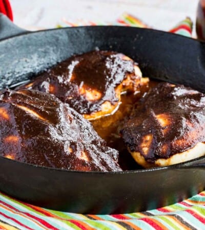 three chicken breasts covered with barbecue sauce in a cast iron skillet