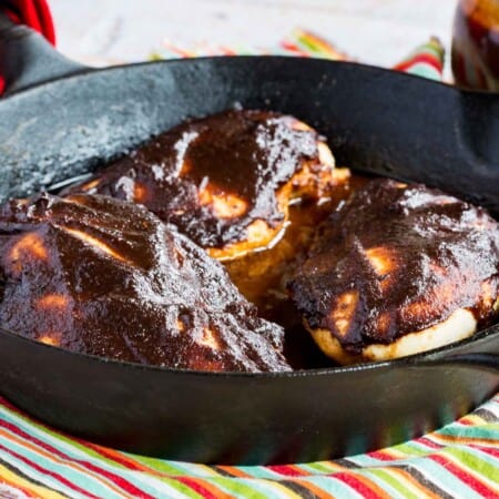 three chicken breasts covered with barbecue sauce in a cast iron skillet