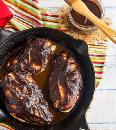 three baked chicken breasts covered in BBQ sauce in a skillet next to a jar of balsamic barbecue sauce
