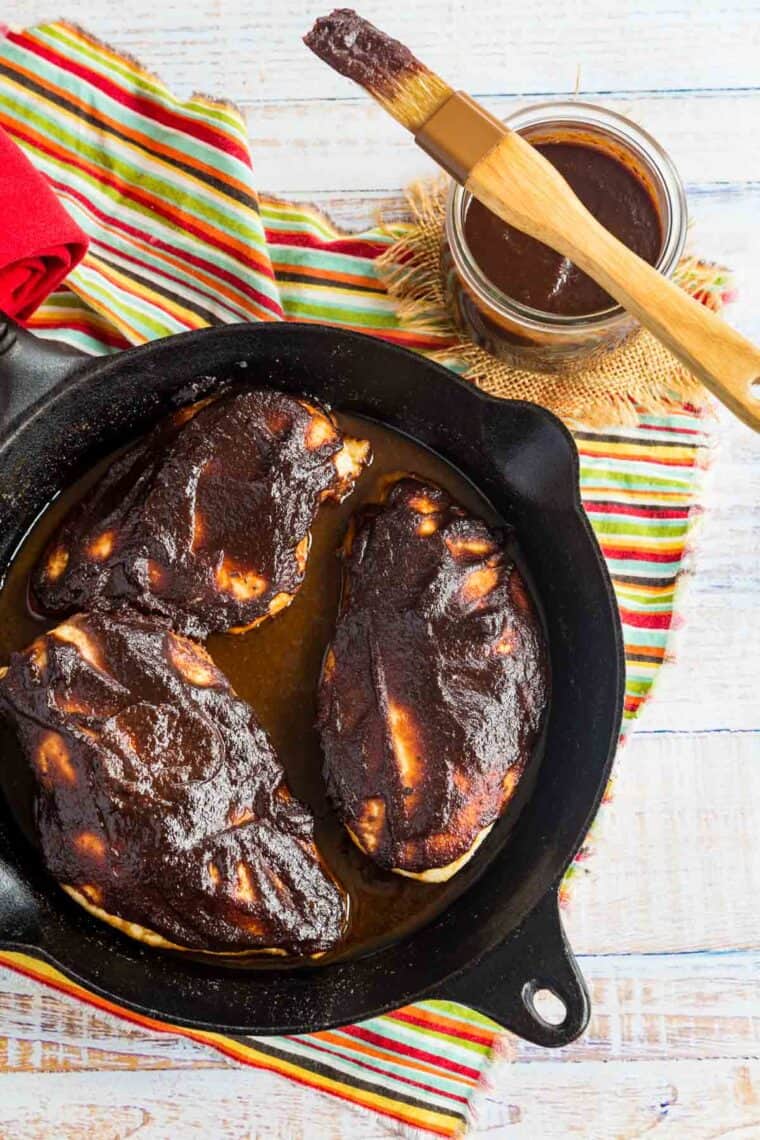 three baked chicken breasts covered in BBQ sauce in a skillet next to a jar of balsamic barbecue sauce