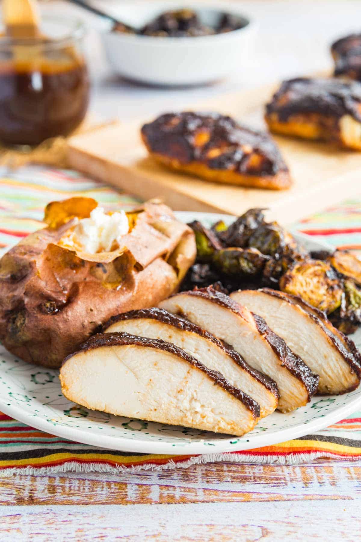 sliced of juicy chicken on a plate serve with a baked sweet potato and brussels sprouts