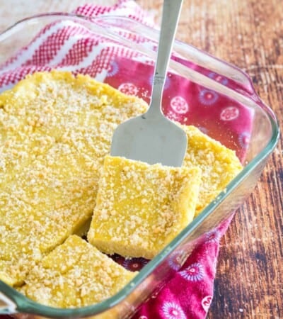 baked polenta cut into squares in a baking dish with one lifted with a serving spatula