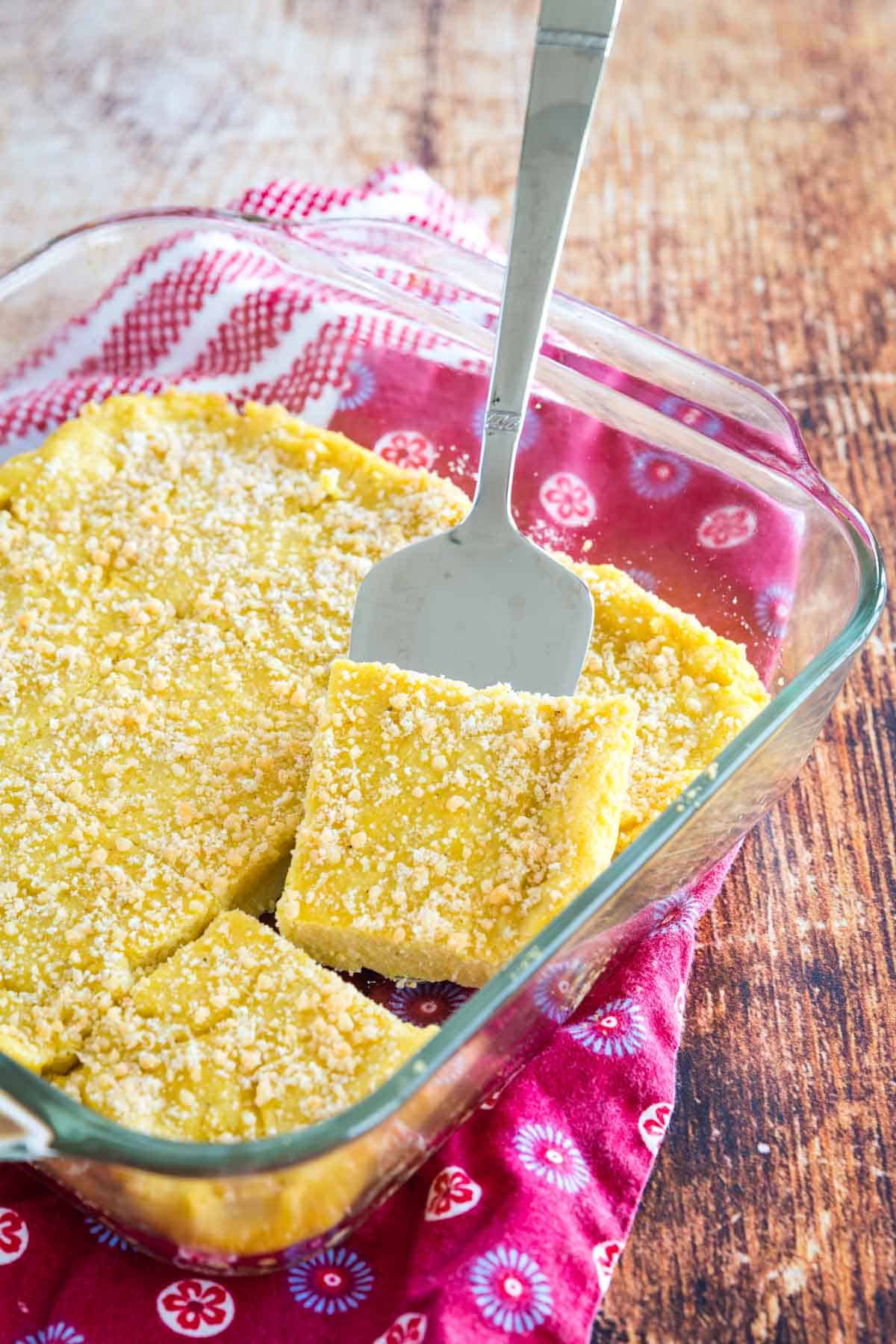 baked polenta cut into squares in a baking dish with one lifted with a serving spatula