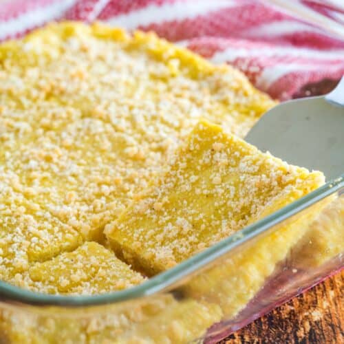 A silver serving utensil lifting a piece of baked polenta with parmesan cheese on top.