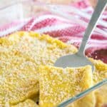 A silver spatula lifting a square of polenta from a glass baking dish with text overlay that says "Parmesan Baked Polenta".