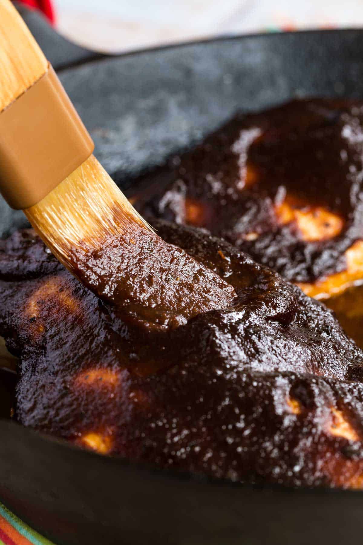 brushing sauce onto bbq chicken in a cast iron skillet