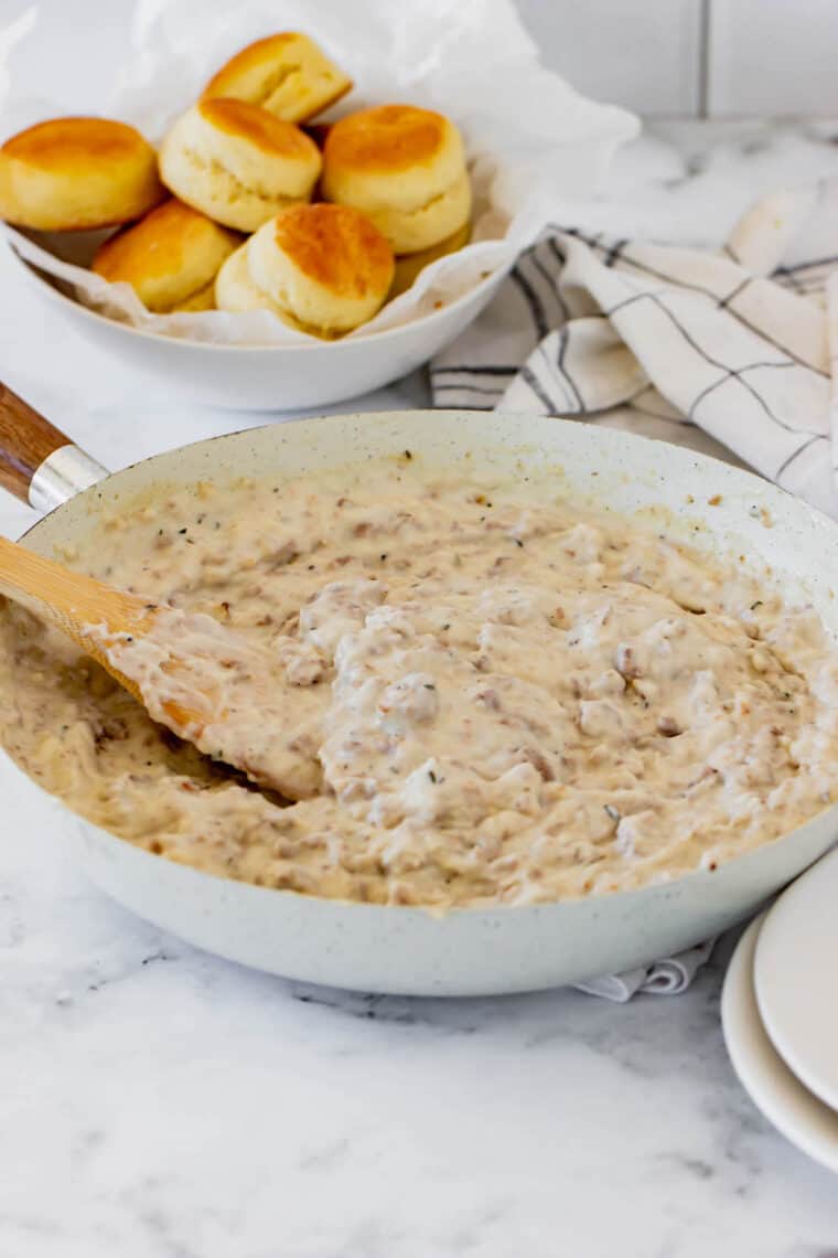 A Skillet Filled with Sausage Gravy Next to a Parchment-Lined Bowl of Biscuits