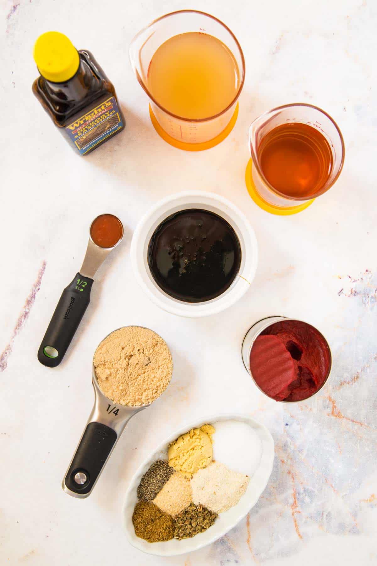 bowls and measuring cups with tomato paste, bourbon, apple cider vinegar, brown sugar, molasses, hot sauce, and different spices and seasonings, and a bottle of liquid smoke