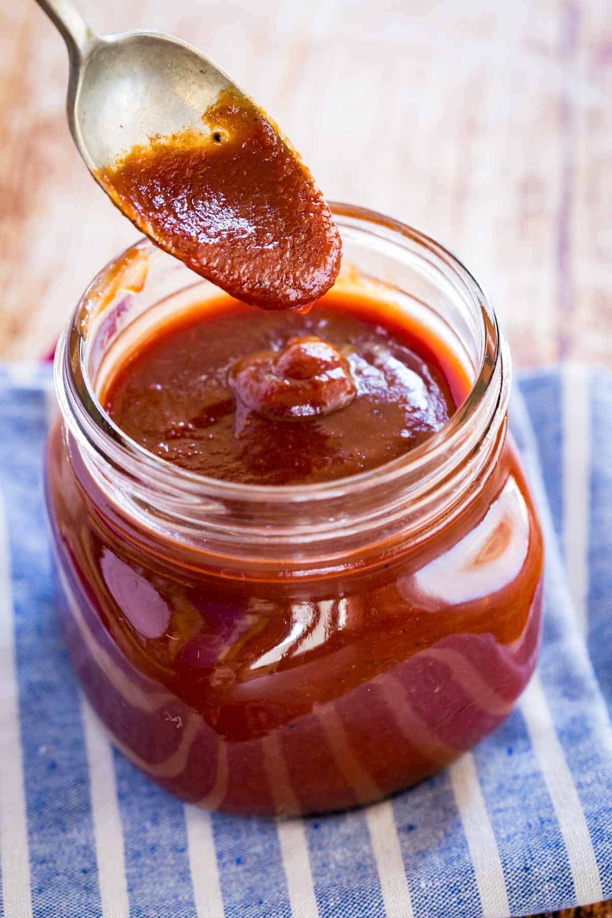 bourbon bbq sauce dripping off of a spoon into a glass jar