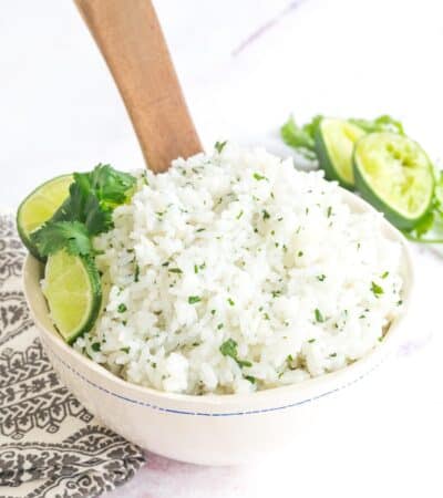 wooden spoon sitting in a bowl of cilantro lime rice garnished with lime slices and cilantro leaves