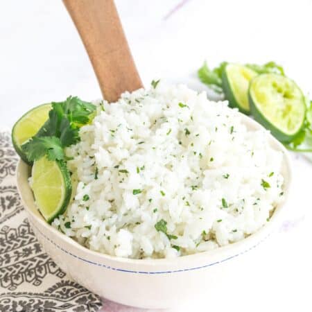 wooden spoon sitting in a bowl of cilantro lime rice garnished with lime slices and cilantro leaves