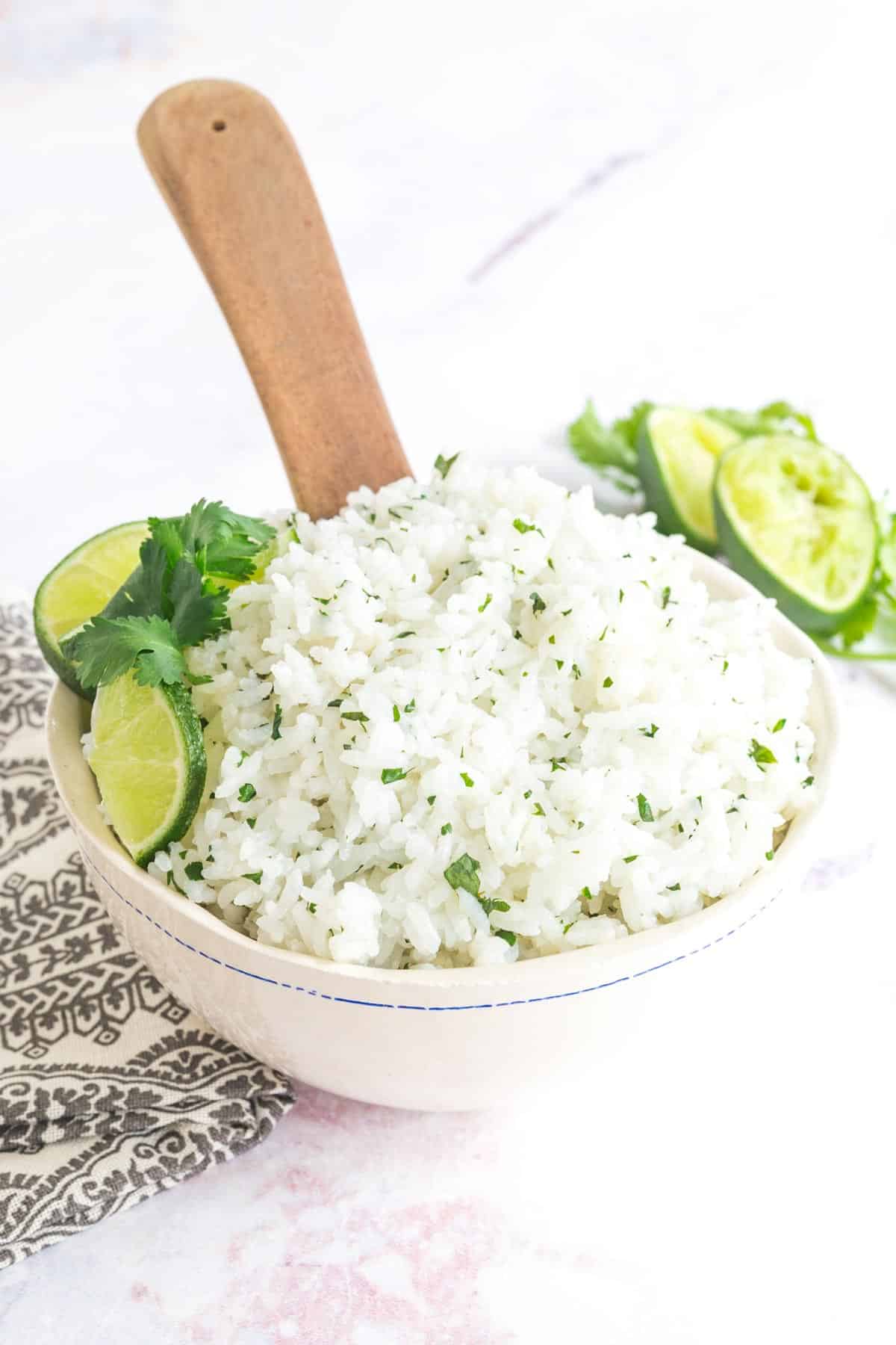 wooden spoon sitting in a bowl of cilantro lime rice garnished with lime slices and cilantro leaves