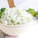 white rice with cilantro flecked through it in a bowl with a wooden spoon and cilantro and lime as garnish