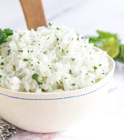 white rice with cilantro flecked through it in a bowl with a wooden spoon and cilantro and lime as garnish