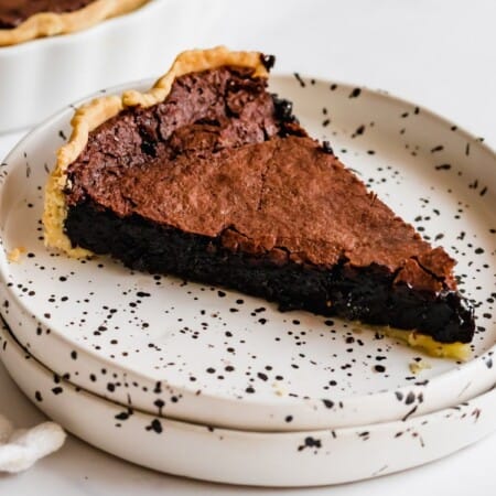 slice of gluten free chocolate chess pie on a white plate with black speckles