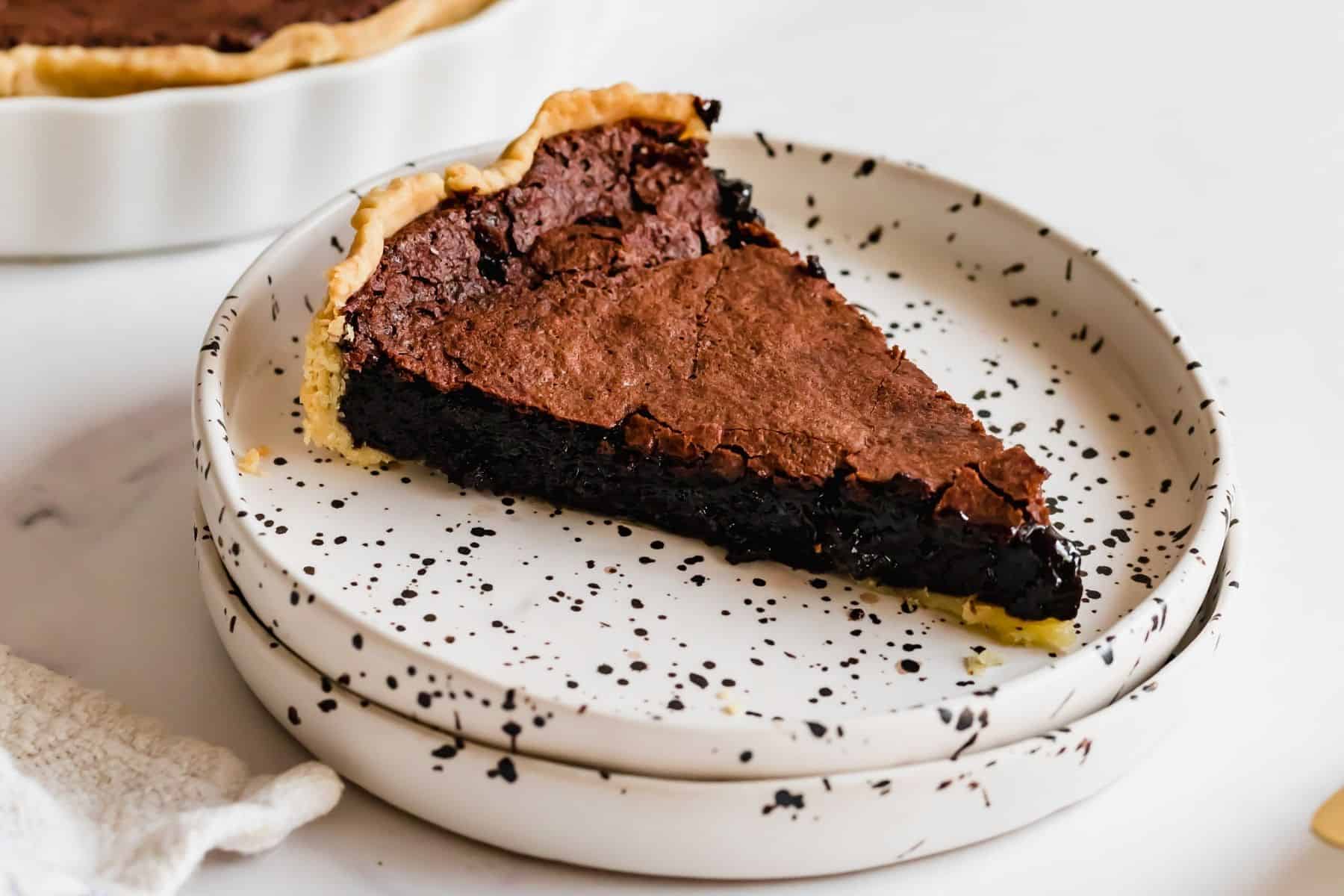 A slice of gluten free chocolate chess pie on a white plate with black speckles.
