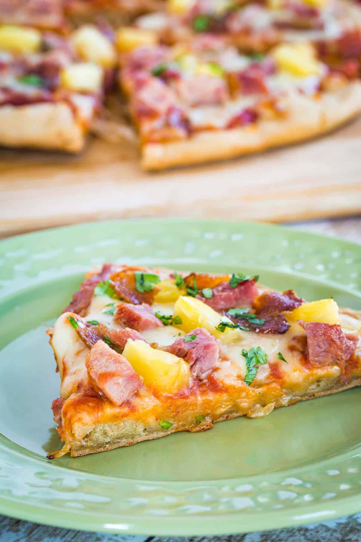 slice of ham and pineapple pizza on a green plate